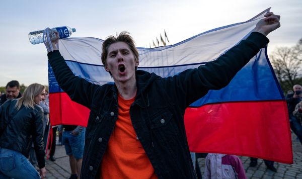 Молодой человек с российским флагом на церемонии возложения цветов у мемориального комплекса "Памятник воинам Советской Армии - освободителям Советской Латвии и Риги от немецко-фашистских захватчиков" в Риге