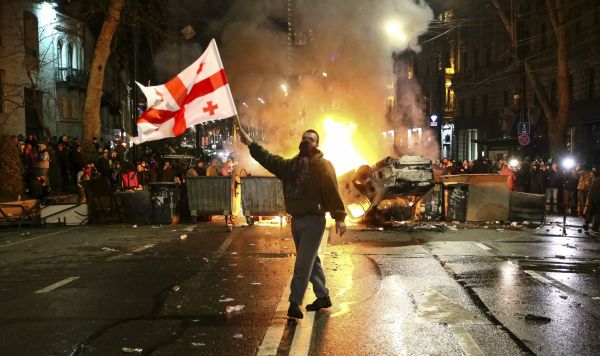 Мужчина с флагом Грузии перед горящей баррикадой у здания парламента в Тбилиси, Грузия, 9 марта 2023