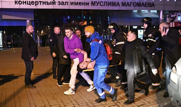 Раненую женщину несут к машине скорой помощи во время теракта в "Крокус Сити Холле", 22 марта 2024